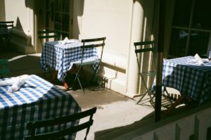 Uteservering med blåvitrutiga dukar och svarta bistrostolar